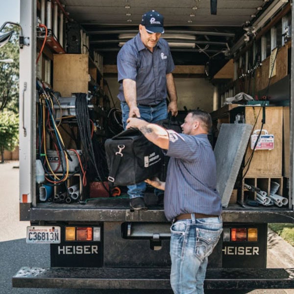 2 Puyallup HVAC technicians unloading branded company truck at job site.