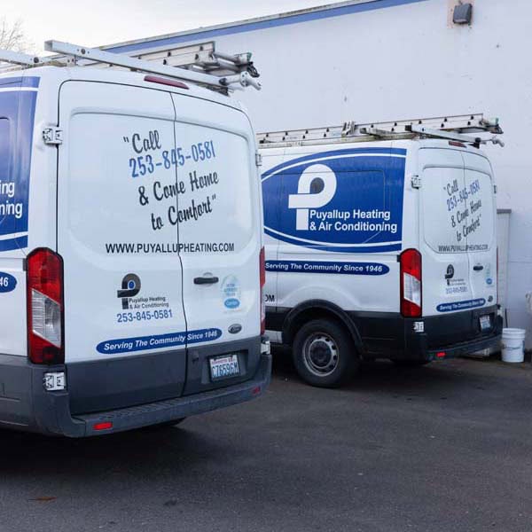 Puyallup Heating & Air Conditioning branded work trucks sitting in a parking lot.