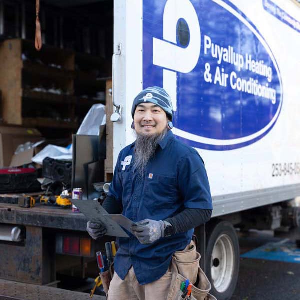 Puyallup Heating & Air Conditioning technician in front of branded work truck sitting in parking lot.