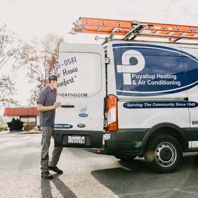 Puyallup HVAC technician looking into back of company branded truck.