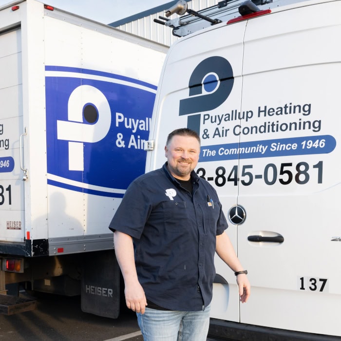 Puyallup HVAC technician standing in front of branded work trucks in parking lot.